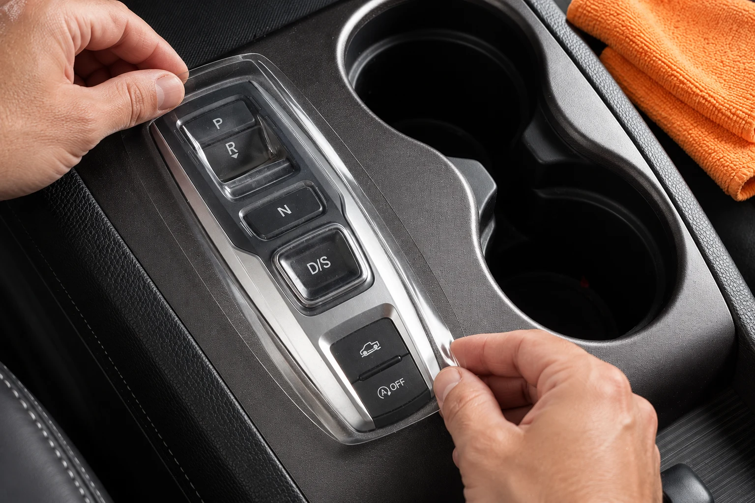 Illustration of hands positioning a transparent molded cover above a parked vehicle’s shifter