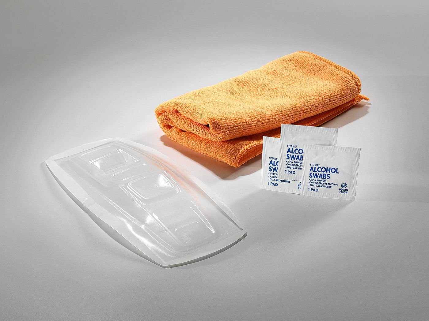 The Button Covers kit: a clear molded cover, an orange microfiber towel and three alcohol prep pads